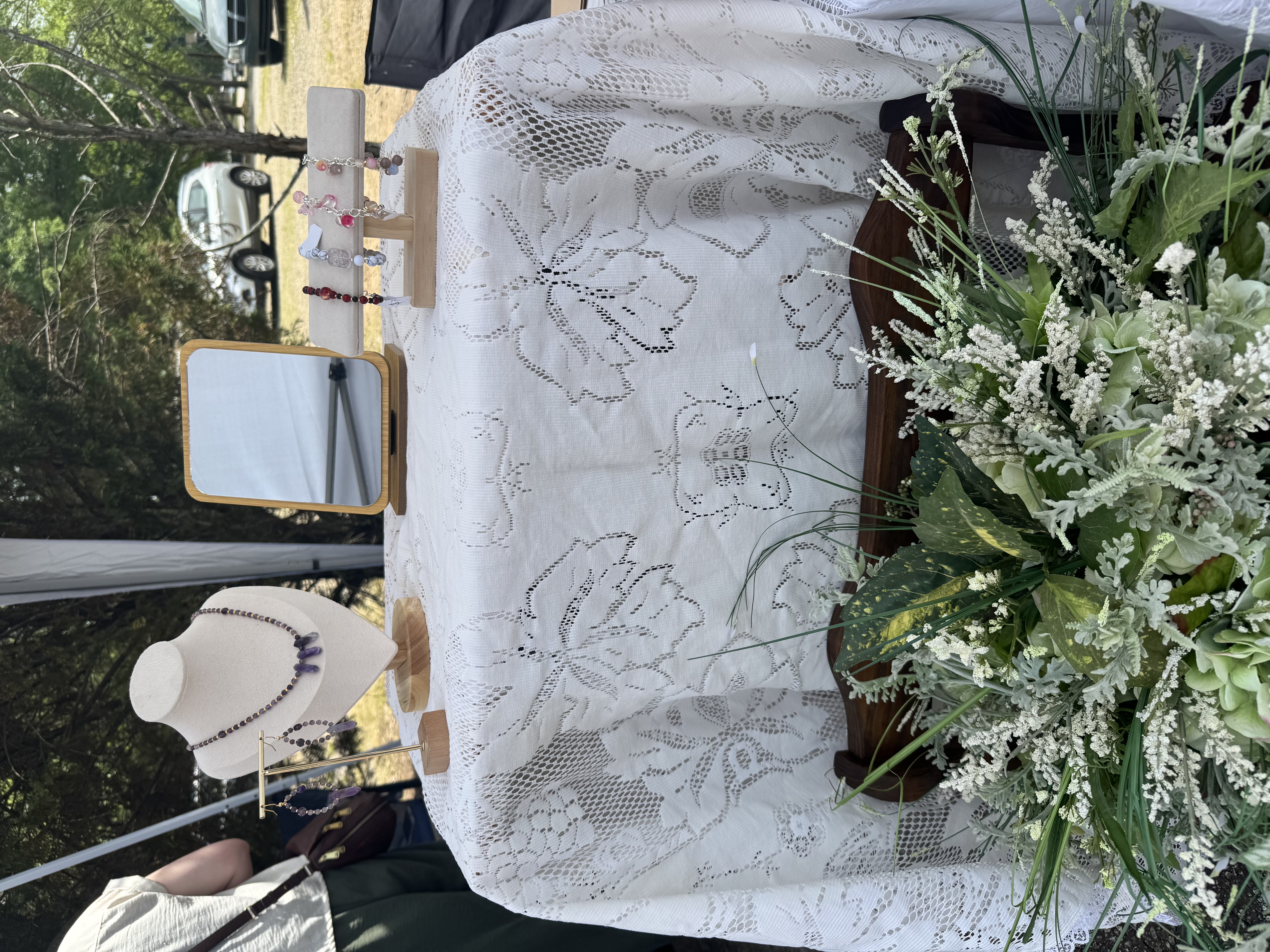 Anne Marie's market booth — lace tablecloth, bracelets, and fresh flowers
